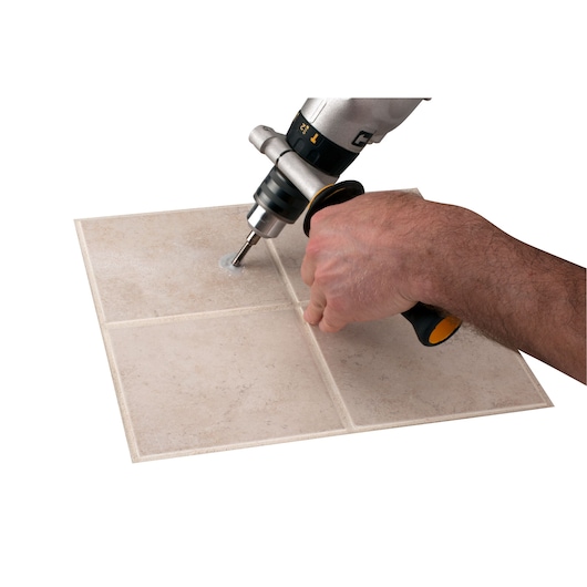 LENOX 1211212DGDS drill bit making hole in ceramic tile, close-up view of hand holding power drill.