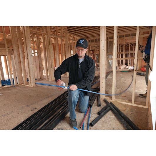 LENOX 12121S1 pipe cutter used by worker cutting blue plastic pipe on construction site with wood framing.