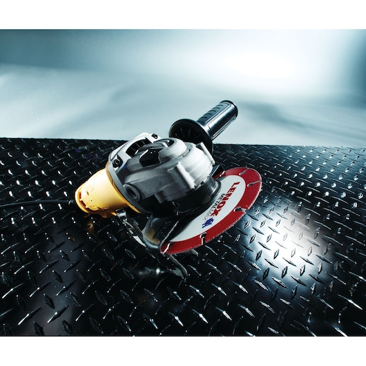Photo of LENOX 1972921 circular saw blade attached to a grinder, shown cutting black diamond plate metal.