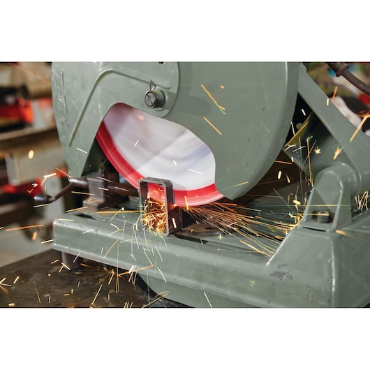 LENOX cutting wheel 1972932 on metal chop saw, side angle, producing sparks while cutting metal pipe.