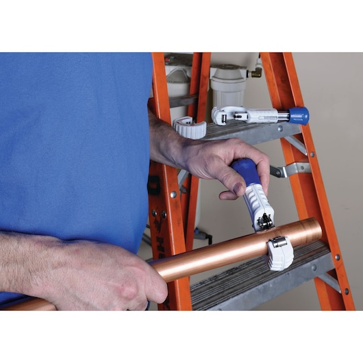 LENOX pipe cutter 21008TC58 held by person, copper pipe being cut, orange ladder and tools visible in background.