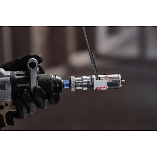 LENOX 3001818l hole saw attached to a drill, gloved hand holding tool, close-up view.