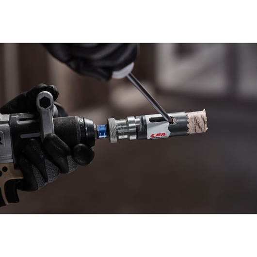 LENOX 3001818l hole saw attached to power drill, gloved hand using screwdriver to remove wood plug.