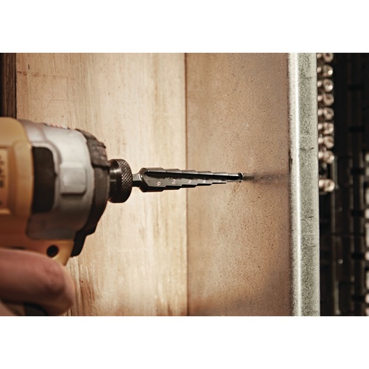 LENOX 30884VB4 step drill bit attached to power drill, drilling into metal sheet, side view.