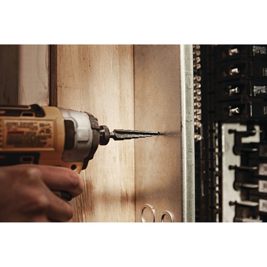 LENOX step drill bit 30884VB4 attached to a power drill making a hole in a metal panel, close-up view.