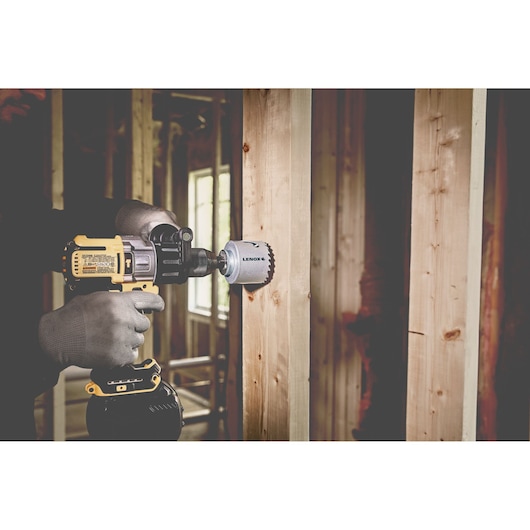 LENOX LXAH3112 hole saw attached to drill cutting through wooden stud, indoor construction setting.