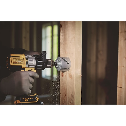 LENOX LXAH3112 hole saw attached to a drill cutting through wood stud, indoor workshop setting.