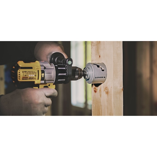 Photo of LENOX LXAH3112 hole saw attached to a power drill cutting through a wooden beam.