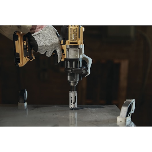 LENOX LXAH3118 hole saw attached to a power drill cutting through metal, worker wearing safety gloves.