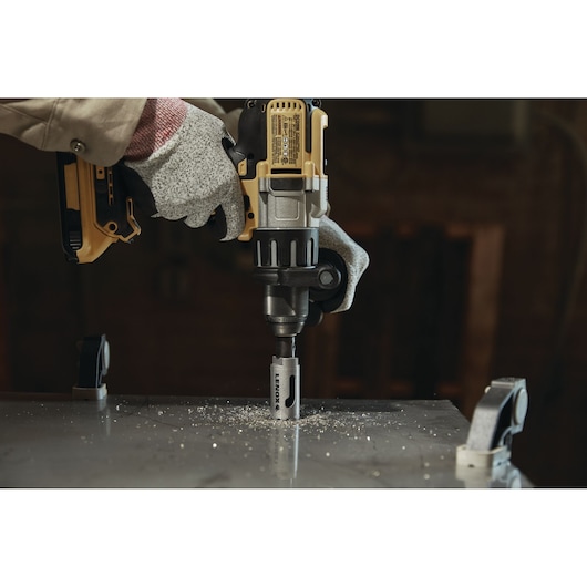 Photo of LENOX hole saw LXAH3118 attached to drill cutting through metal sheet with gloved hand.
