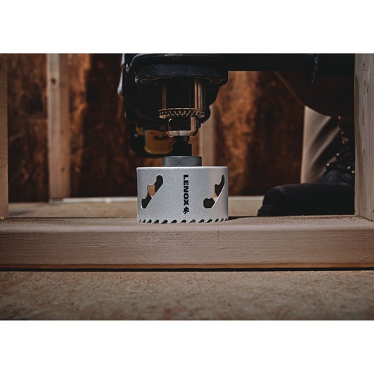 Photo of LENOX hole saw LXAH3212 mounted on a drill, cutting through wood in a construction setting.