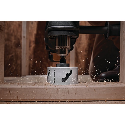 Photo of LENOX LXAH3212 hole saw attached to a drill cutting through wood with sawdust flying.
