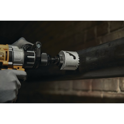 LENOX LXAH3212 hole saw attached to a power drill cutting through a metal pipe, close-up view.