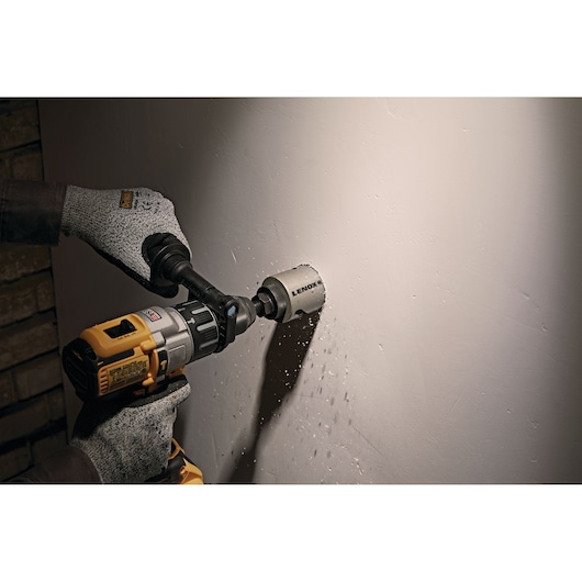 LENOX LXAH3218 hole saw drilling into a white wall, attached to a power drill, photography.