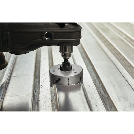 LENOX LXAH3412 hole saw attached to drill cutting through metal sheet, close-up side angle.
