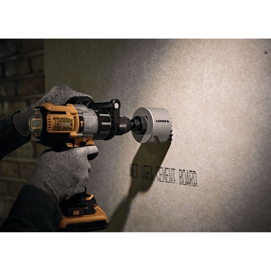 Photo of LENOX LXAH3 hole saw attached to a drill, cutting a circular hole in a drywall panel.