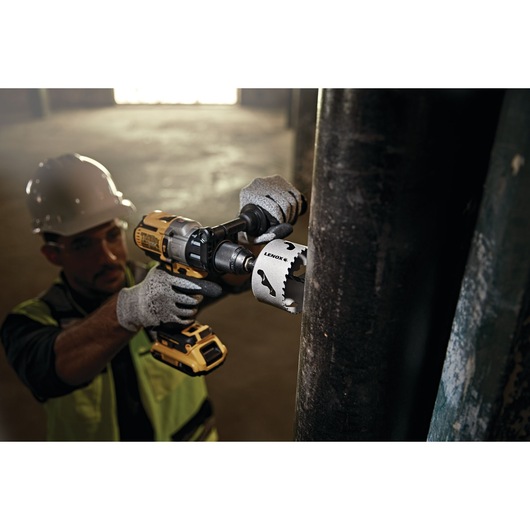 LENOX LXAH3 hole saw attached to power drill cutting through a large metal pipe in industrial setting.