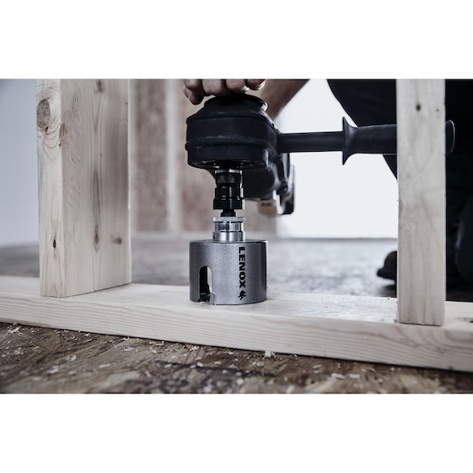 Photo of LENOX LXAH4358 hole saw attached to a power drill cutting through wood in a construction setting.