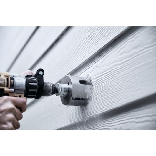 LENOX LXAH4358 hole saw drilling into wood siding, close-up side angle, dust visible.