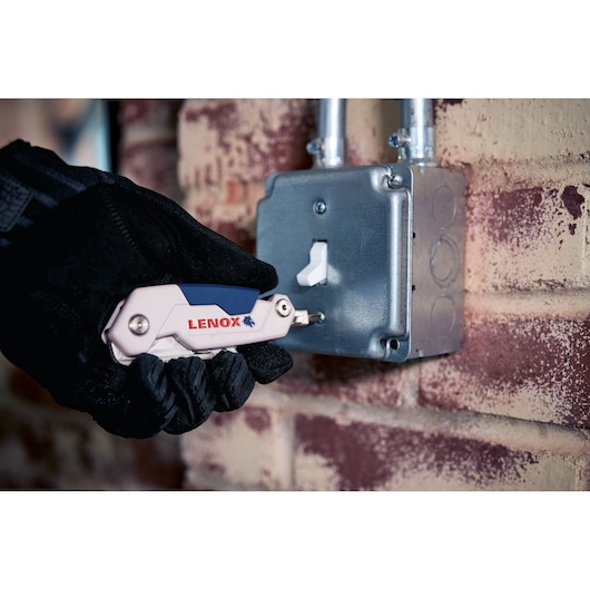LENOX LXHT10601 multi-tool screwdriver used by a gloved hand on a metal electrical box near a brick wall.