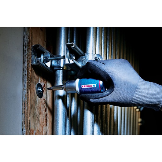Photo of LENOX LXHT60901 screwdriver with blue grip used by gloved hand to fasten screw on metal clamp.