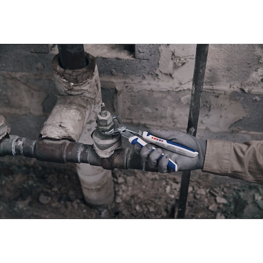 Photo of LENOX adjustable wrench LXHT90551 in use tightening a pipe fitting, glove hand, industrial setting.