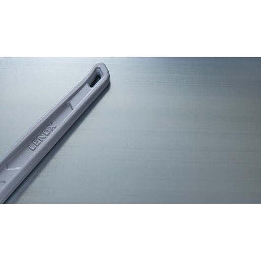 Photo of LENOX LXHT90624 gray metal handle with embossed logo, partial view on metallic background.