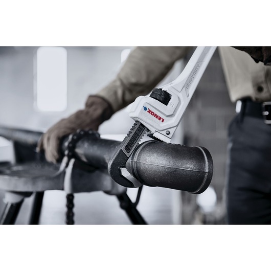 Photo of a LENOX pipe wrench LXHT90714 gripping a metal pipe in an industrial setting.